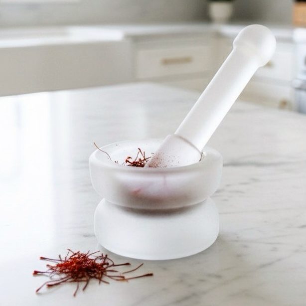 Crystal Mortar and pestle with saffron strands on a marble surface.
