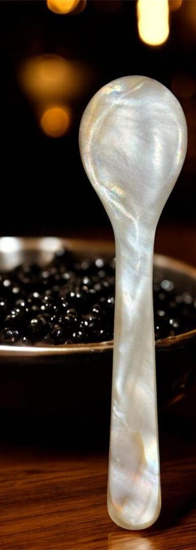 A decorative spoon made of mother-of-pearl beside a bowl of black beads.