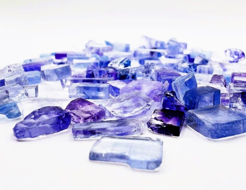 Translucent violet and blue Salt crystals scattered on a white surface.
