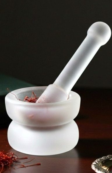 Crystal mortar and pestle with crushed red saffron on a wooden surface.
